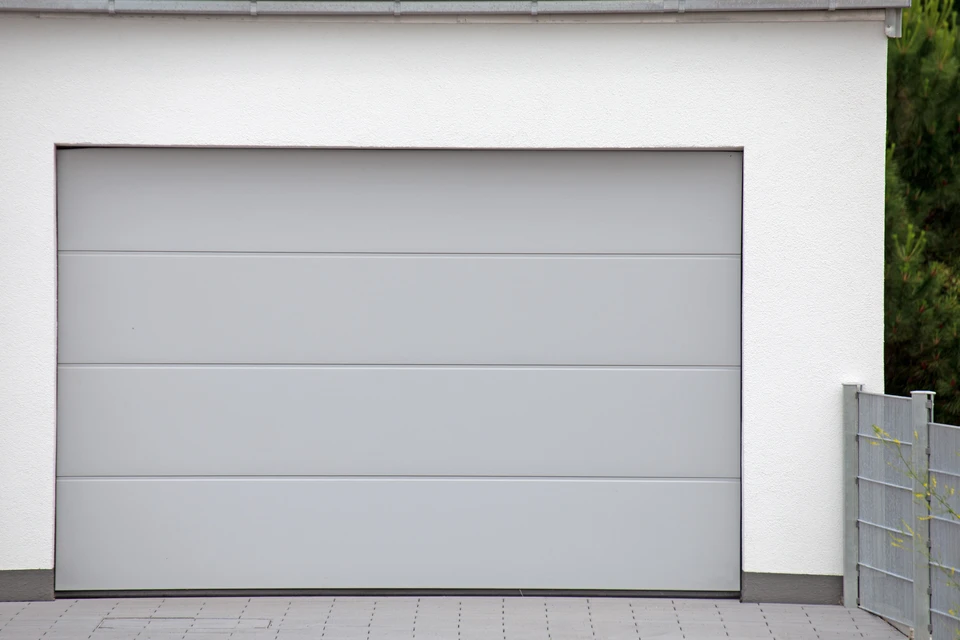 Extérieur résidentiel moderne avec porte de garage sectionnelle grise à quatre panneaux horizontaux lisses, intégrée dans façade blanche contemporaine