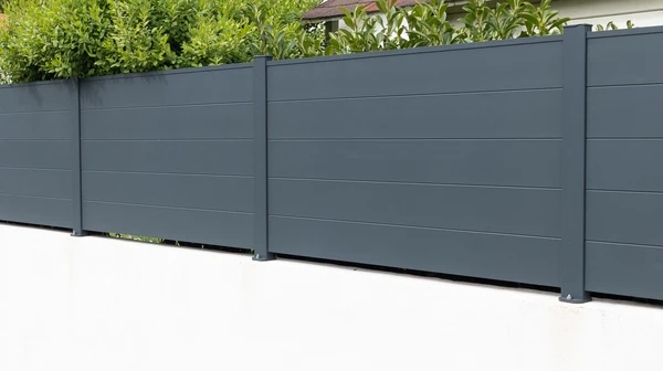 Scène extérieure résidentielle montrant une clôture moderne installée le long d'une allée pavée claire
